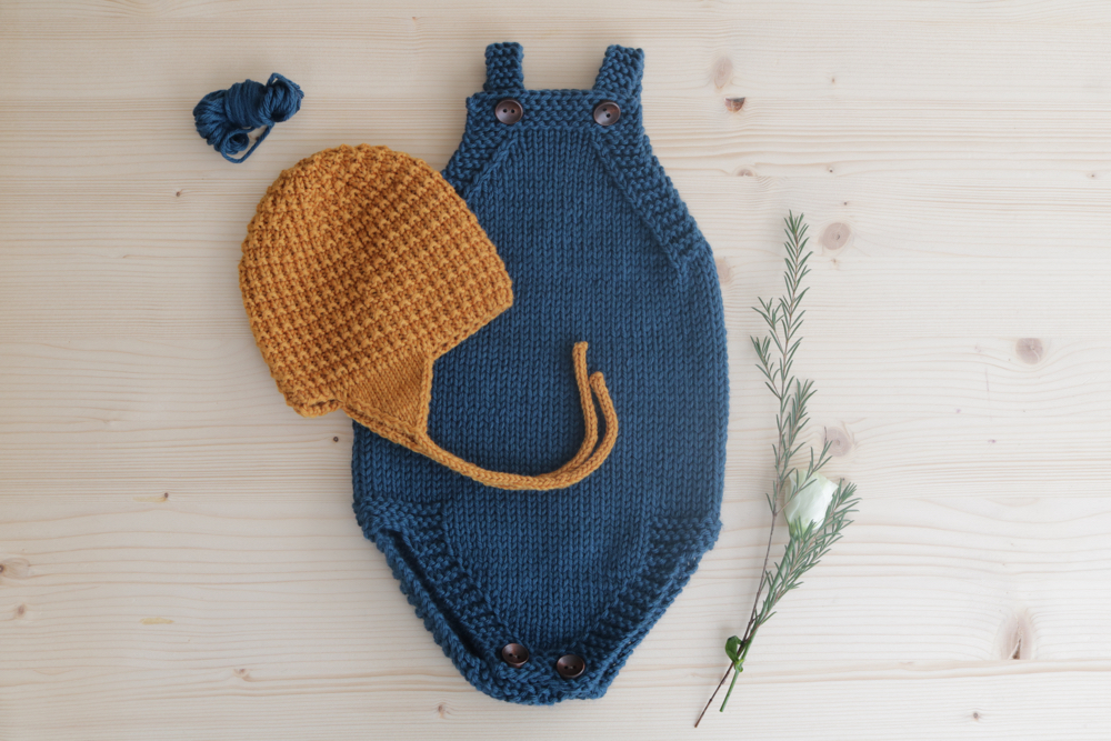 dunkelblauer Babystrampler und karamellfarbene Babymütze mit Garnrest und Blümchen
